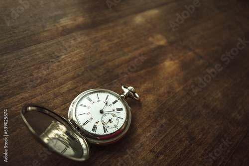 Vintage round pocket watch on a wooden table. Nostalgia for a bygone time.