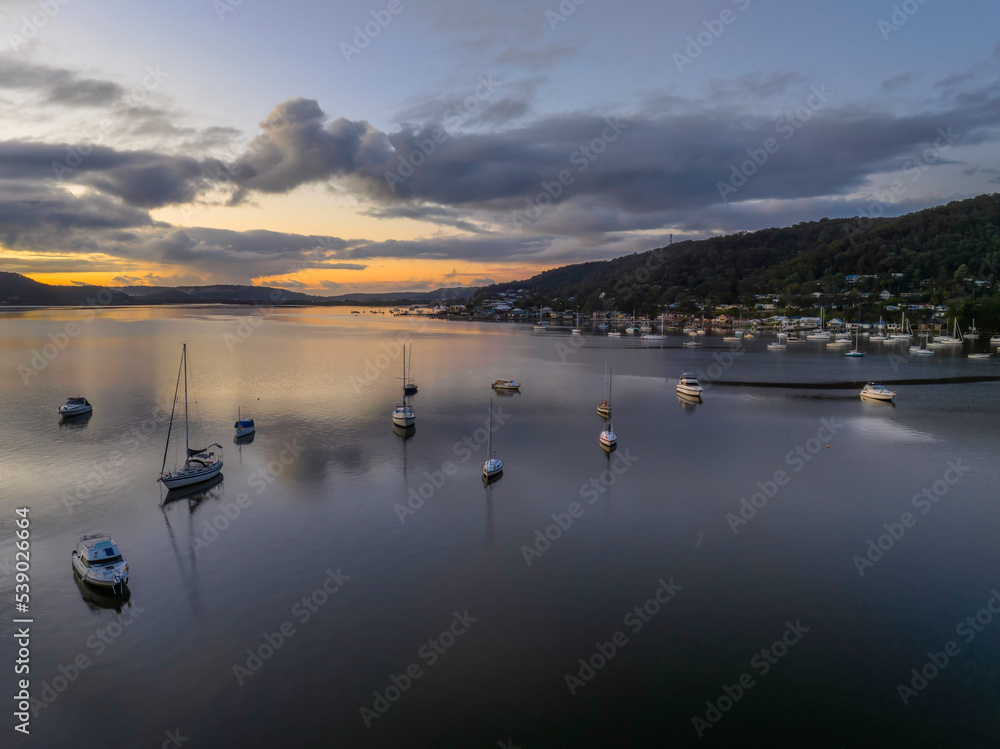 Fototapeta premium Aerial sunrise waterscape with boats, rain clouds and reflections