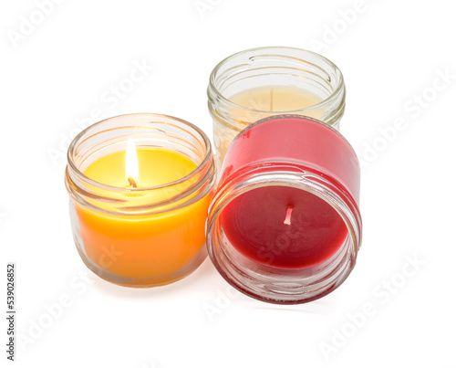 a set of multicolored scented candles with one lit in glass jars on a white background