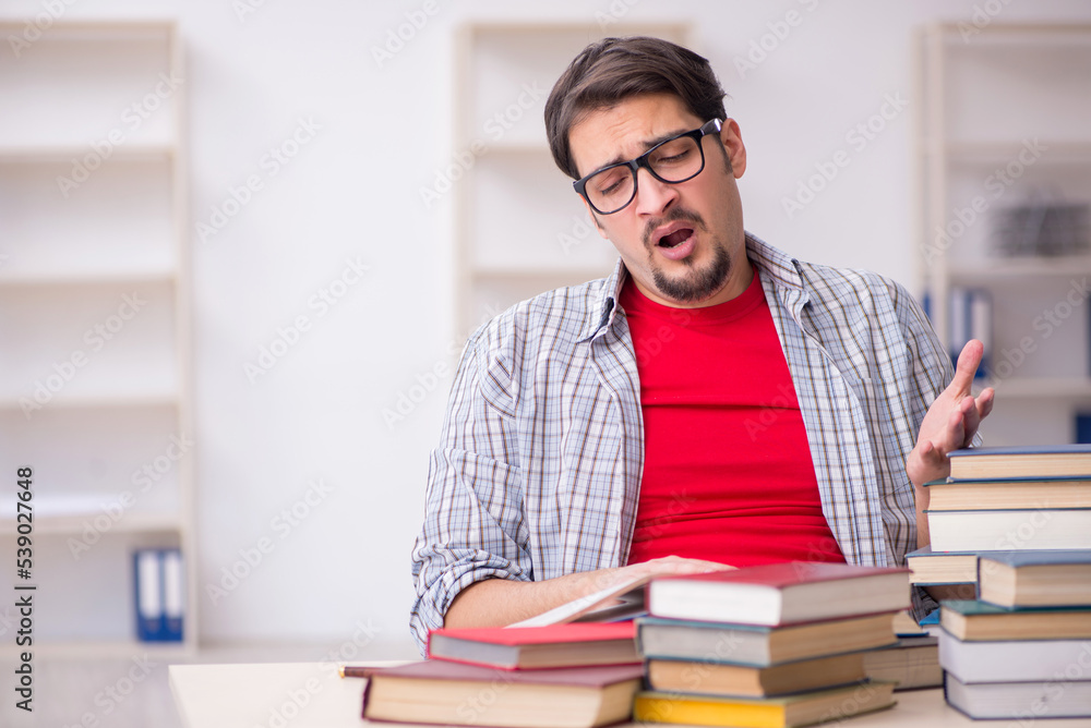 Young male student and too many books in the classroom Young male student and too many books in the classroom
