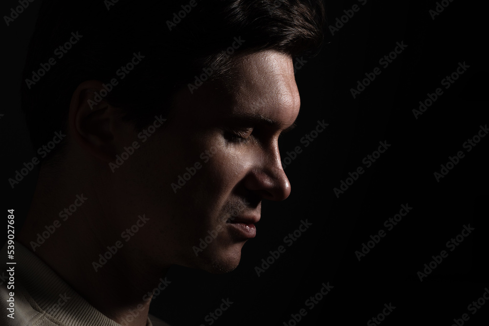 profile of thoughtful man looks to the right. portrait in side light, hard light, photo on black, looks down profile of thoughtful man looks to the right. portrait in side light, hard light, photo on black, looks down