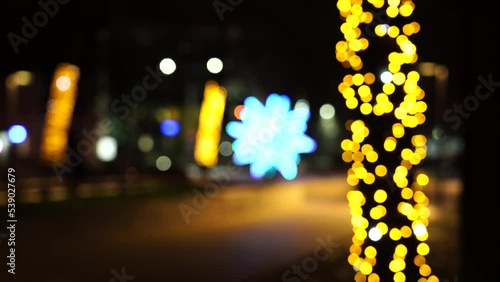 New Year's illumination of blurred yellow balls on trees on the street, square. Road and cars