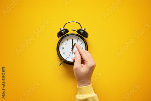 Daylight saving day. Fall Back. Black Alarm clock and female hands on yellow background. Daylight saving time end