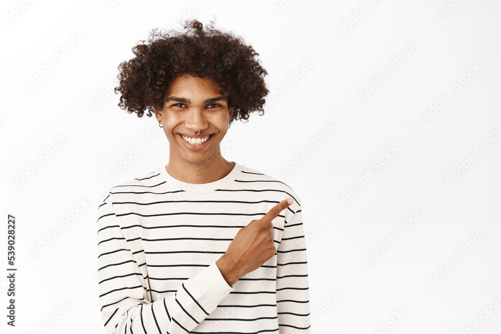 Close up portrait of young hispanic guy pointing finger right, showing advertisement, promo offer, announcement banner aside, standing over white background Close up portrait of young hispanic guy pointing finger right, showing advertisement, promo offer, announcement banner aside, standing over white background