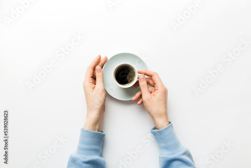 Minimalistic style woman hand holding a cup of coffee on Colored background. Flat lay, top view espresso cup. Empty place for text, copy space. Coffee addiction. Top view, flat lay