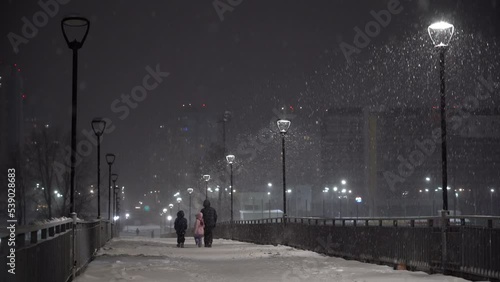 Family, dad and children walk down the street in winter with lanterns on the background of snowfall