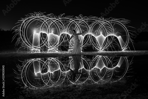 Woman posing for light painting with bright lights in the dark. Reflection in the water