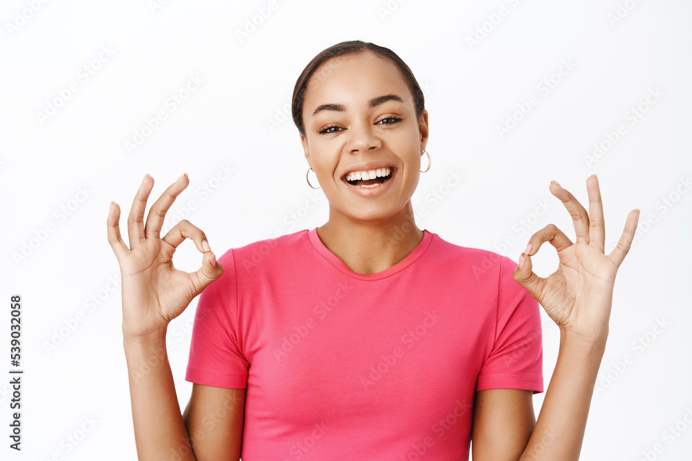 Close up of smiling happy woman, shows okay sign and say yes, approve smth, recommends, praising smth good. stands over white background Close up of smiling happy woman, shows okay sign and say yes, approve smth, recommends, praising smth good. stands over white background