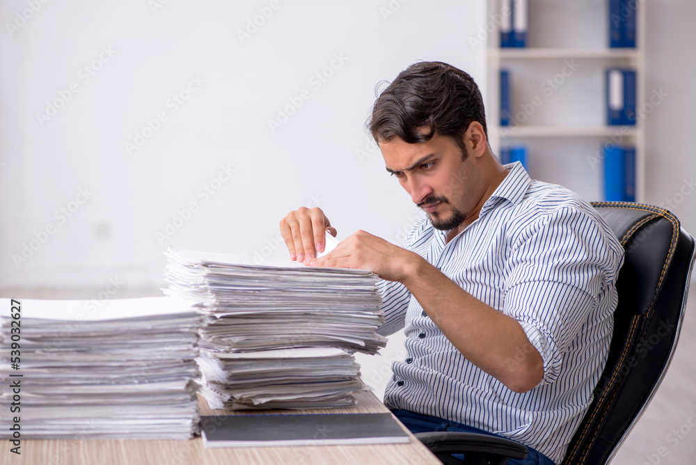 Young male employee unhappy with excessive work in the office Young male employee unhappy with excessive work in the office