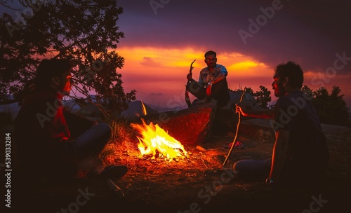 People sitting around a campfire in the wild, at sunset.