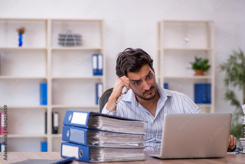 Young male employee unhappy with excessive work in the office Young male employee unhappy with excessive work in the office