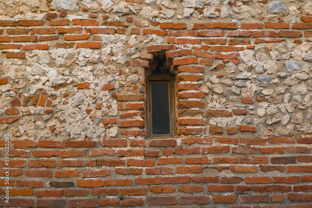 An arched window in a fortress or castle made of red stone. Architecture of old stone buildings. Window in the wall. Window with an arch of an old castle. An arched window in a fortress or castle made of red stone. Architecture of old stone buildings. Window in the wall. Window with an arch of an old castle.