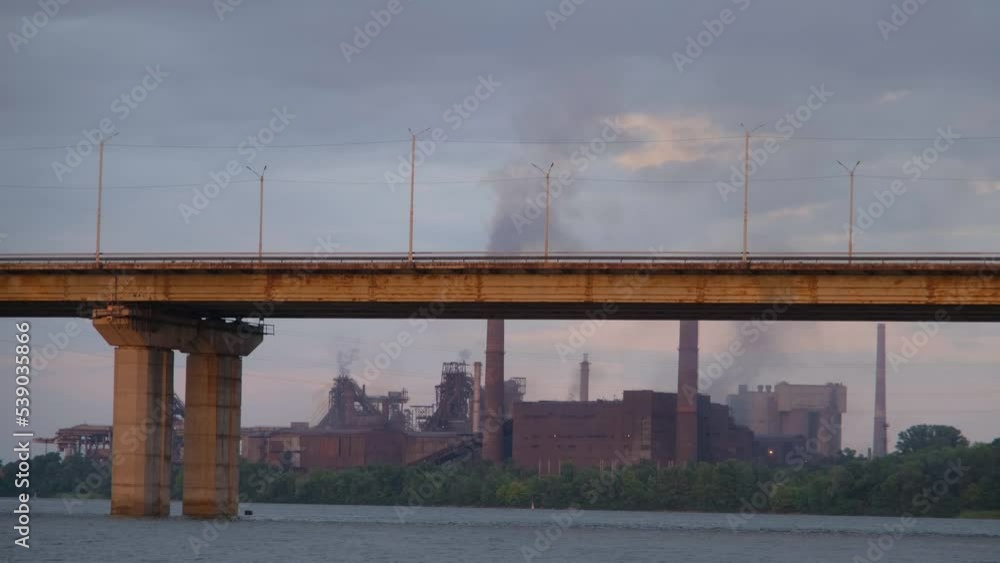Factory with a smoking chimney near the river. Smoking factory at sunset. Dramatic landscape at sunset Factory with a smoking chimney near the river. Smoking factory at sunset. Dramatic landscape at sunset