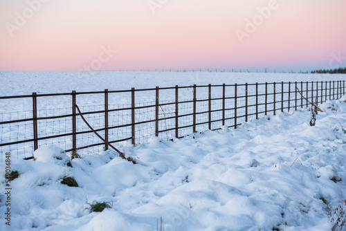 A fence under a red sky during sunset in a Winter day in the Pentland Hills Regional Park in Edinburgh, Scotland, UK, with the ground covered in snow © CarlosGLopez
