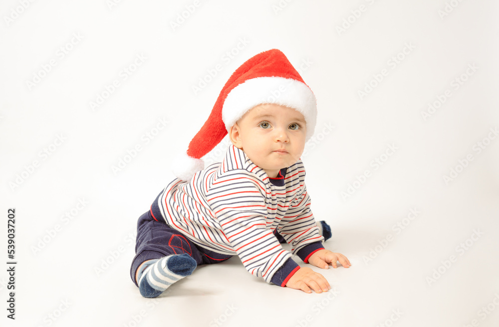 Adorable child is sitting on floor, wearing red Christmas cap, isolated over white background. Adorable child is sitting on floor, wearing red Christmas cap, isolated over white background.