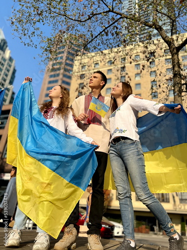 two girls, one guy in embroidered National clothes with Ukrainian flags waving them war is over Ukraine's victory They cover the camera with a flag in front of the camera, yellow blue flashes