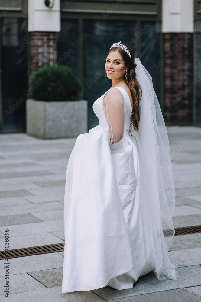 A beautiful, smiling bride in a white dress walks in the city, in the park against the backdrop of buildings. Wedding photography, portrait. A beautiful, smiling bride in a white dress walks in the city, in the park against the backdrop of buildings. Wedding photography, portrait.