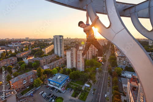 Rock climber hanging on element of roof of high building at sunset. photo