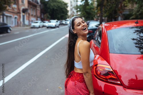 Portrait of pretty Caucasian woman standing against new red car