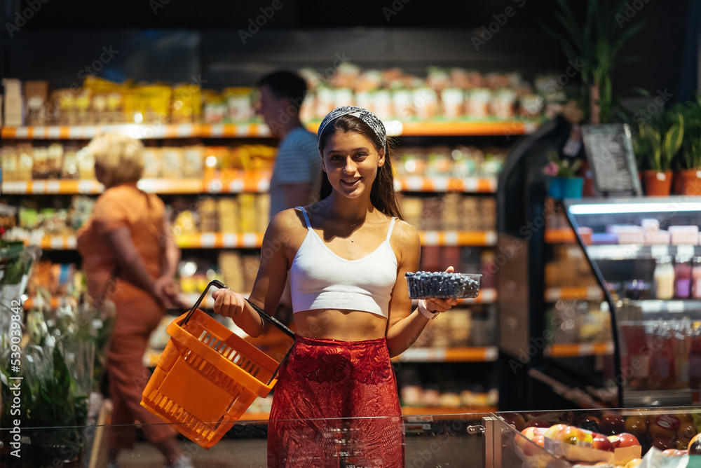 Fototapeta premium young woman do shopping in supermarket. choosing blueberry in store