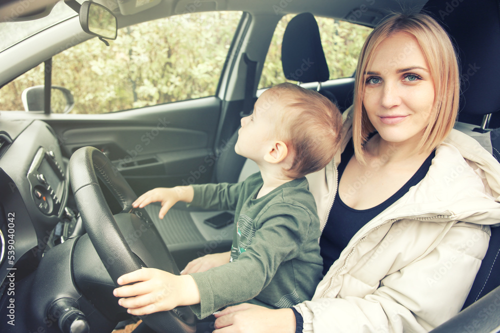 A small child sits in his mother's arms holding the steering wheel. Children in the car. Love little boys machines