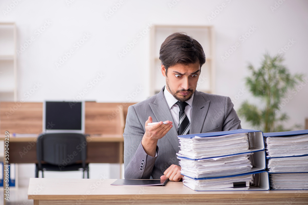 Young male employee unhappy with excessive work in the office Young male employee unhappy with excessive work in the office