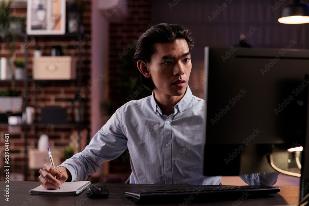 Male employee taking notes on files, working on paperwork documents to plan business report remotely from home. Analyzing information and data online on website, using computer. Male employee taking notes on files, working on paperwork documents to plan business report remotely from home. Analyzing information and data online on website, using computer.