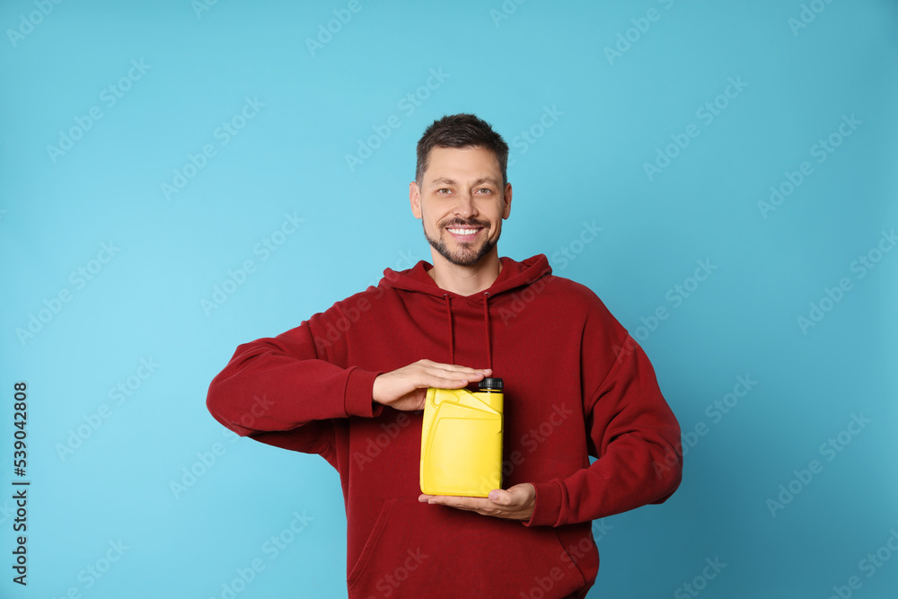 Man holding yellow container of motor oil on light blue background Man holding yellow container of motor oil on light blue background