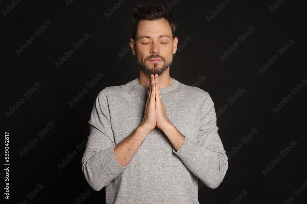 Man with clasped hands praying on black background Man with clasped hands praying on black background
