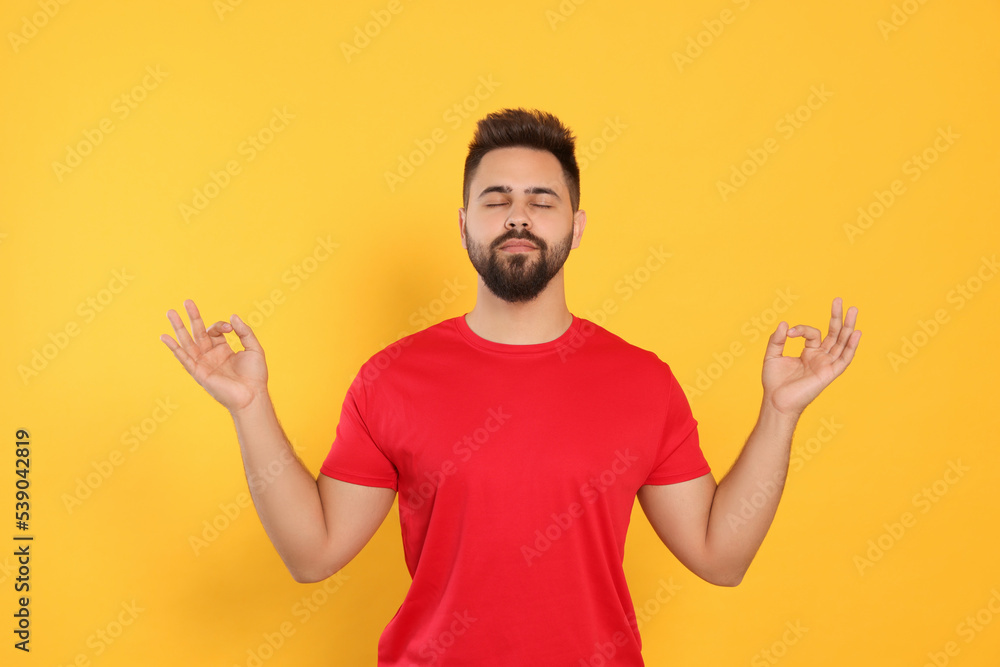 Fototapeta premium Young man meditating on yellow background. Zen concept