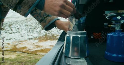 Traveler female in camping on vacation mountain road trip putts ground coffee into stovetop coffee maker. Woman preparing breakfast on weekend journey. Camp life and travel wanderlust freedom photo