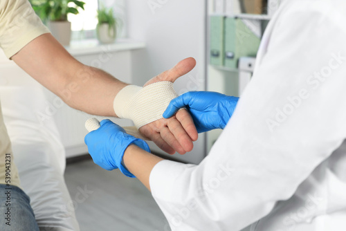 Doctor applying medical bandage onto patient's hand in hospital, closeup photo