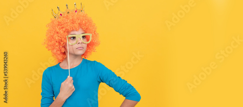 serious teen girl in fancy clown wig wear queen crown and funny party glasses, arrogant. Funny teenager child in wig, party poster. Banner header, copy space.