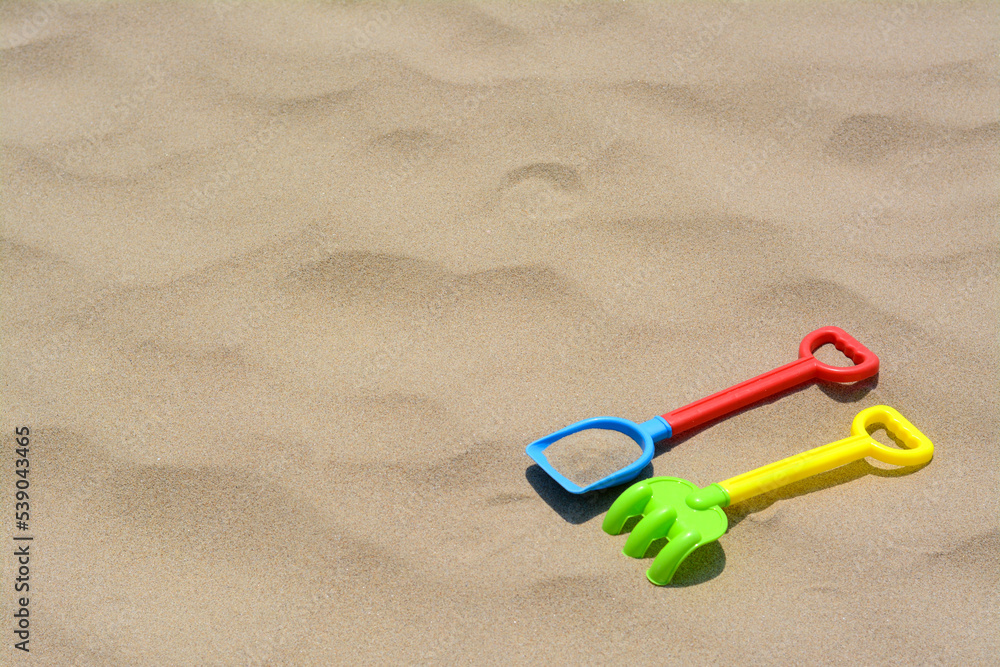 Plastic shovel and rake on sand, space for text. Beach toys Plastic shovel and rake on sand, space for text. Beach toys