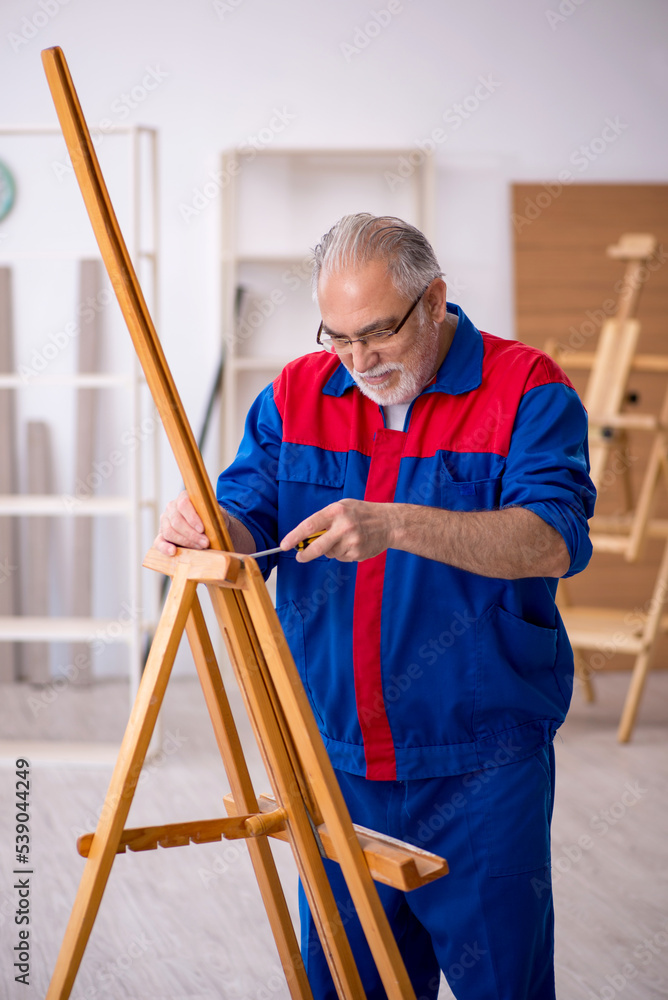Old male carpenter repairing drawing easel Old male carpenter repairing drawing easel