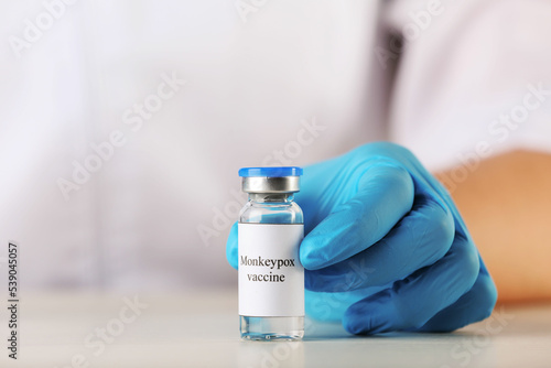 Nurse with glass vial of monkeypox vaccine at table, closeup