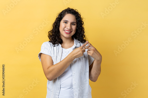 Internet trends. Portrait of woman with dark wavy hair crossing fingers to make hashtag sign and looking at camera with toothy smile. Indoor studio shot isolated on yellow background.
