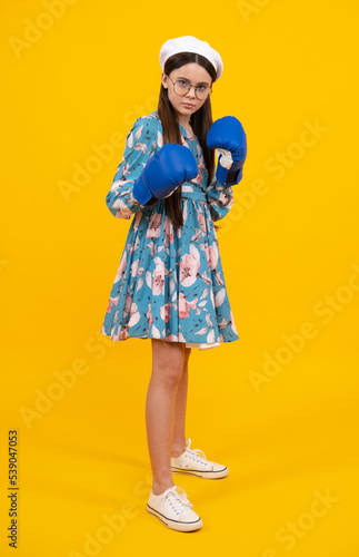 Teenage fun boxer girl in boxing gloves on yellow isolated background. Funny girl boxer in fun gloves boxing, studio shot on yellow. © Olena