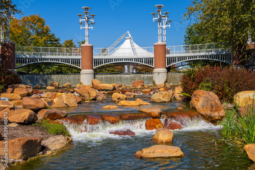 a gorgeous autumn landscape at World's Fair park with a flowing river with green water rushing over smooth brown rocks surrounded by autumn colored trees and lush green trees and grass in Knoxville photo
