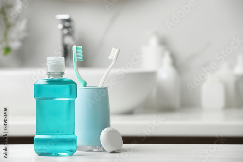 Photos Mouthwash, toothbrushes and dental floss on white countertop in bathroom