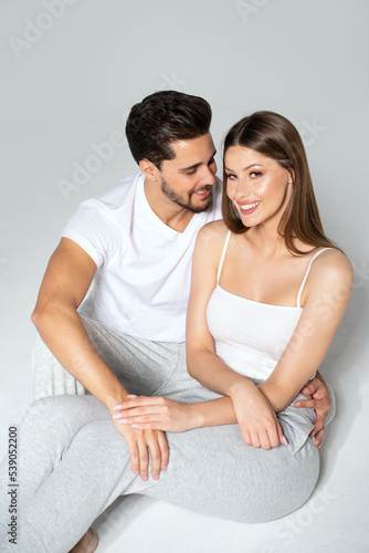 Cheerful young couple sitting and relaxing together, smiling to the camera. Happy woman and man wearing comfortable clothes.