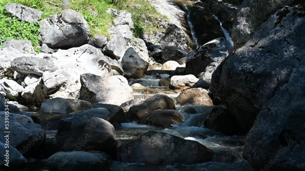 A mountain stream with rocks and a waterfall in the background (slow motion) A mountain stream with rocks and a waterfall in the background (slow motion)