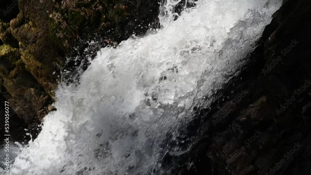 A waterfall between rocks in summer sunlight (slow motion) A waterfall between rocks in summer sunlight (slow motion)
