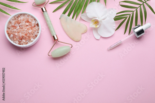 Flat lay composition with gua sha stone and face roller on pink background. Space for text