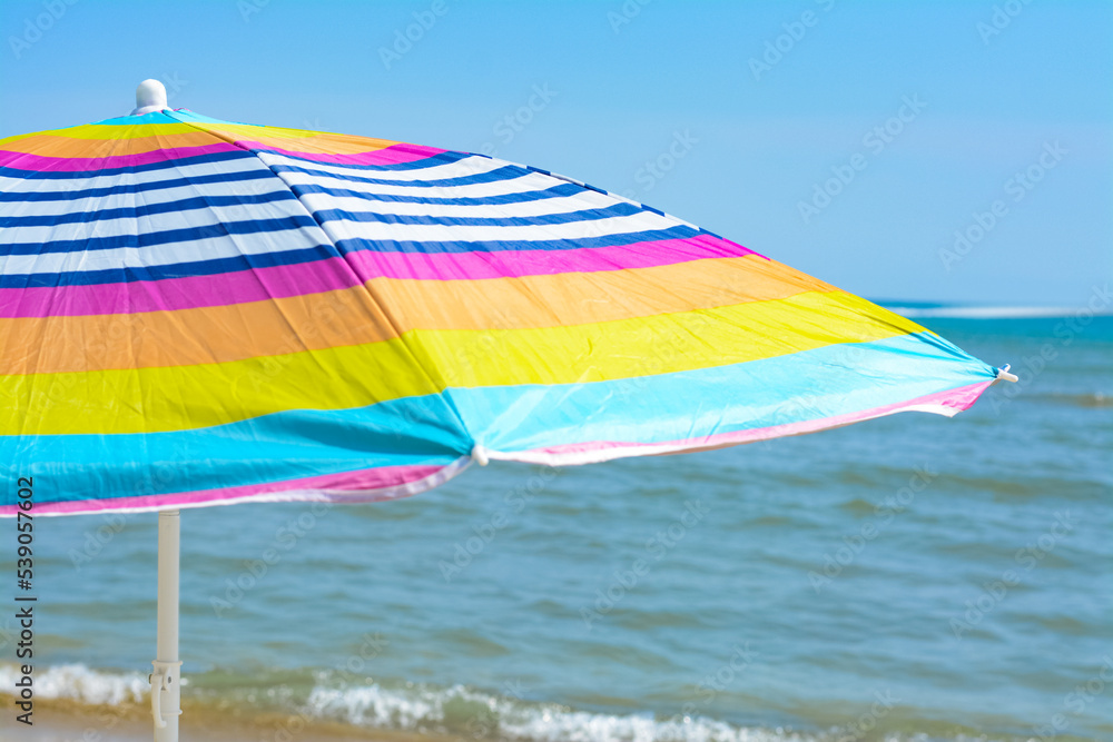 Colorful striped beach umbrella near sea sunny day, closeup