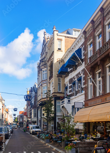 View of historical district of Old Town The Hague overlooking narrow picturesque street with old buildings, shops and open air restaurants on sunny summer day, Netherlands.