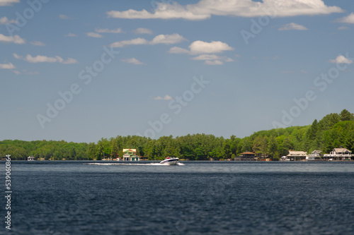 Speeding boat on Lake Joseph in Muskoka, Ontario. Cottagese nestled between green trees are visible