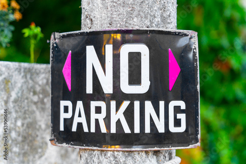 Black and white design No parking sign on metal signboard on concrete pole near park flower beds with green trees. Sign restricting parking in public park in private area photo