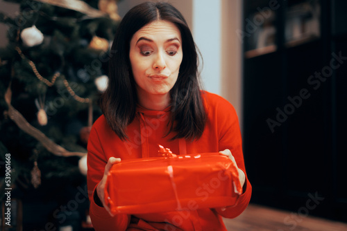 Unhappy Woman Receiving a Gift under the Tree on Christmas. Displeased girlfriend thinking to return the unwanted present
 photo