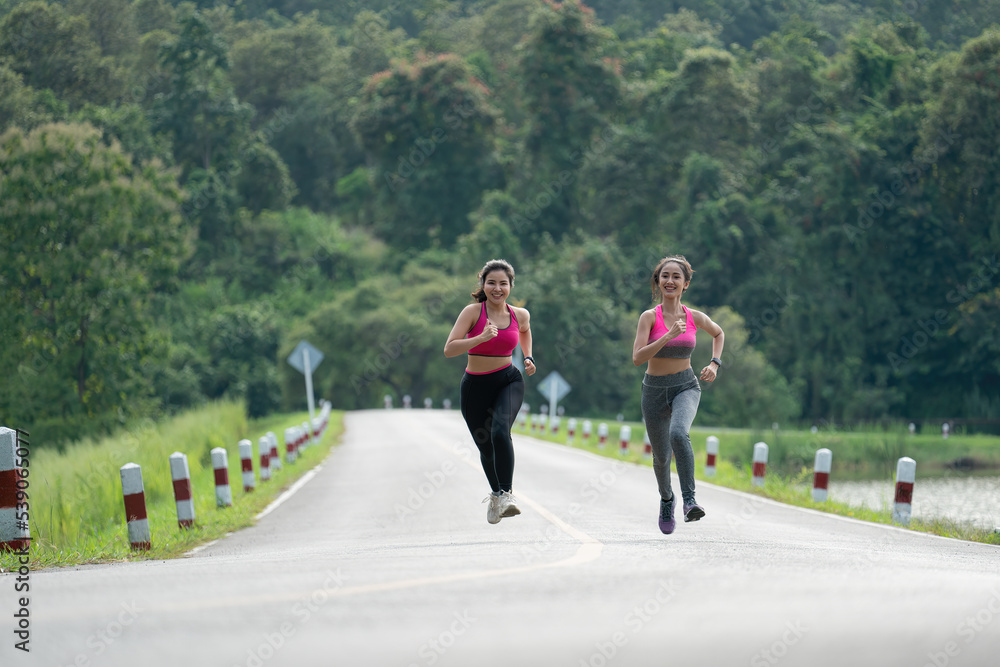 Obraz premium Two Asian women running in the park and smiling.